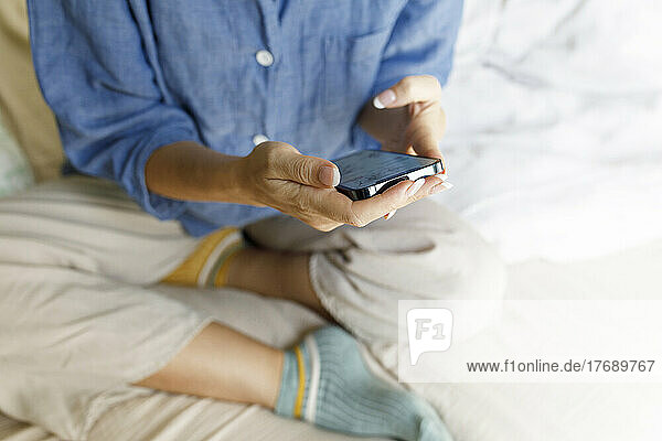 Hands of woman holding mobile phone sitting on bed