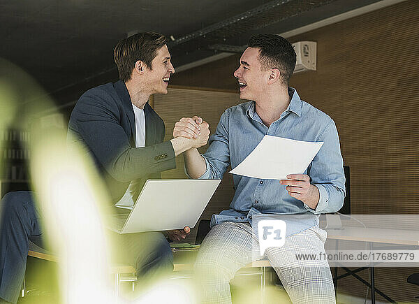 Zwei glückliche Kollegen schütteln sich im Büro die Hand