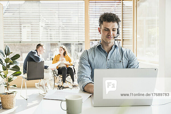 Junger Mann mit Headset und Laptop am Schreibtisch im Büro