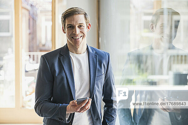 Smiling businessman holding smartphone in office