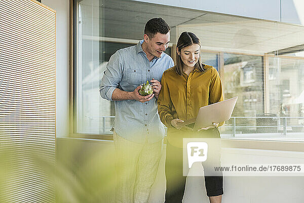 Businessman and businesswoman with laptop and healthy lunch at the window in office