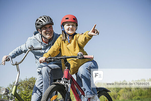 Lächelnder Großvater und Enkelin gestikulieren auf dem Fahrrad sitzend