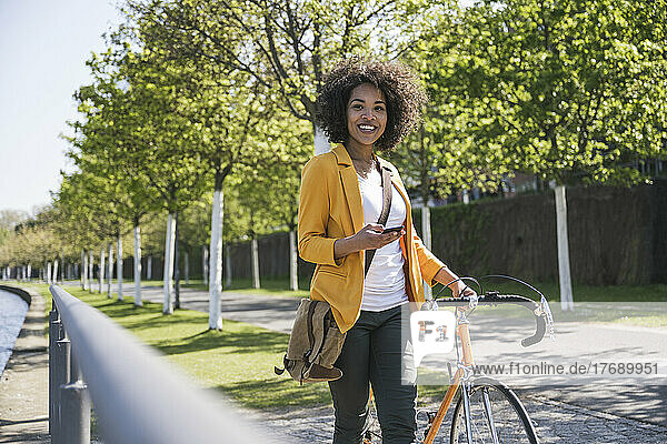 Smiling businesswoman with bicycle on footpath