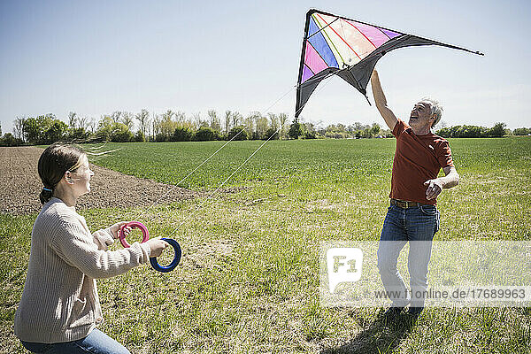 Grandfather teaching granddaughter flying kite on field