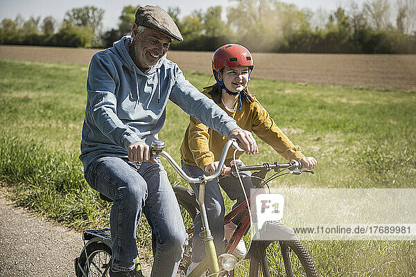Smiling grandfather with granddaughter cycling on sunny day