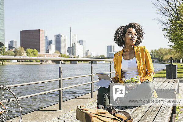 Young businesswoman with laptop sitting on bench by River Main