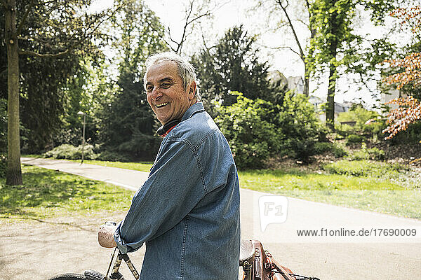 Happy senior man wheeling bicycle on sunny day