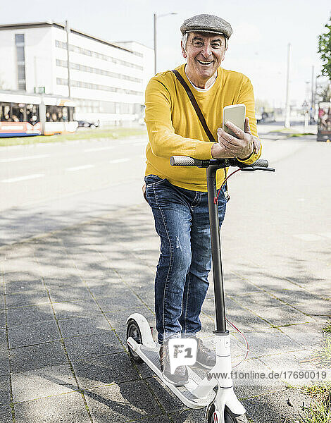 Smiling senior man with mobile phone and electric push scooter on sidewalk