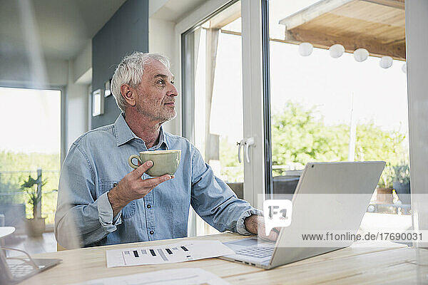 Thoughtful freelancer with coffee cup sitting at home