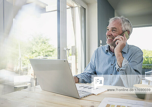 Smiling freelancer talking on smart phone at home