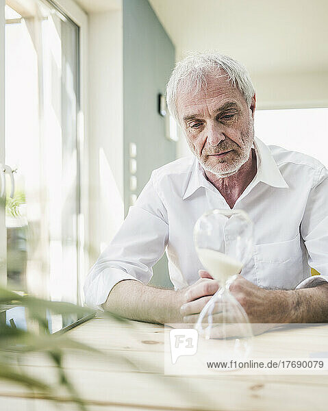 Senior man looking at hourglass on table at home