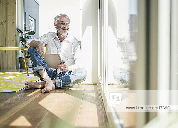 Smiling senior man with tablet PC sitting on floor at home