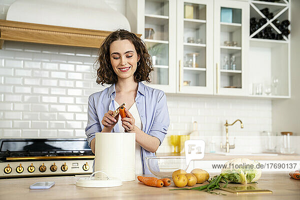 Smiling woman peeling carrot at dining table in kitchen
