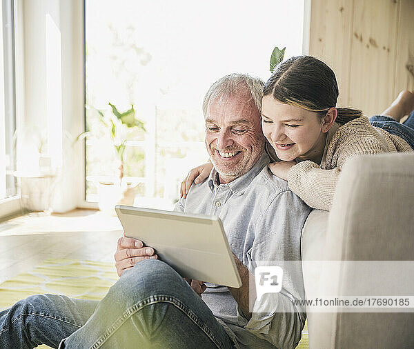 Glücklicher älterer Mann mit Enkelin  der zu Hause einen Tablet-PC nutzt