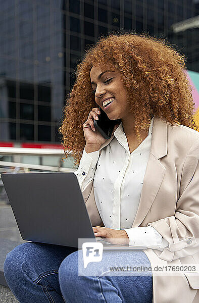 Smiling businesswoman with laptop talking on smart phone