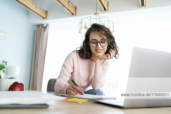 Smiling woman studying and writing in book at home