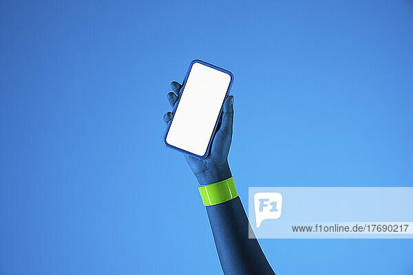 Hand of young woman holding smart phone against blue background