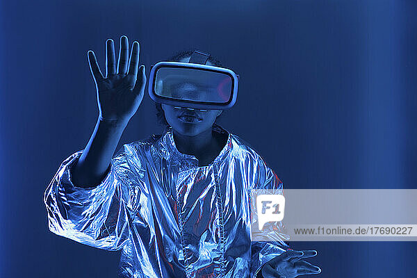 Young woman in virtual reality simulator gesturing against blue background