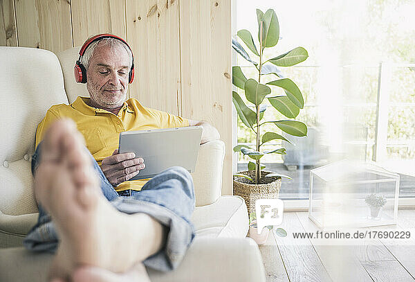 Senior man wearing wireless headphones using digital tablet at home