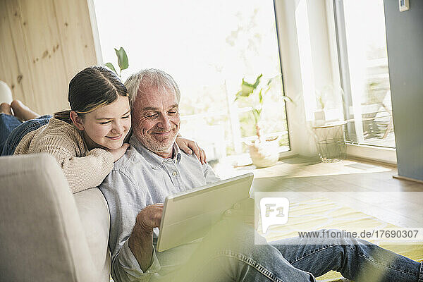 Lächelnder älterer Mann mit Enkelin  der zu Hause einen Tablet-PC nutzt