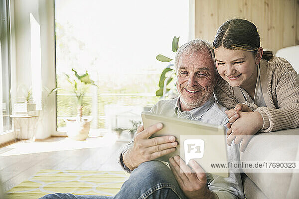 Glücklicher älterer Mann mit Enkelin  der zu Hause einen Tablet-PC nutzt