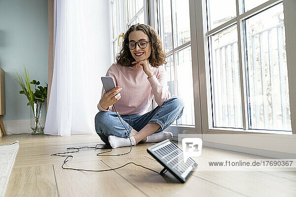 Smiling businesswoman using mobile phone sitting on ground at home