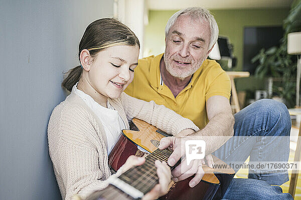 Smiling senior man teaching guitar to granddaughter at home