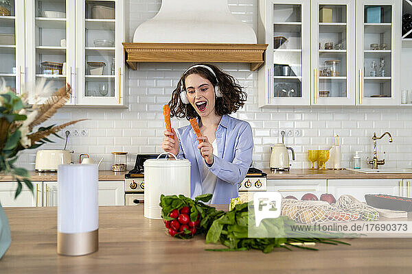 Cheerful woman listening music and playing container with carrots at home
