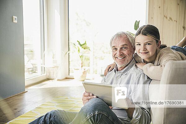 Happy senior man and granddaughter with tablet PC at home