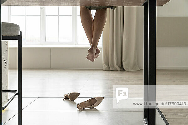 Woman with dangling legs sitting on table in kitchen