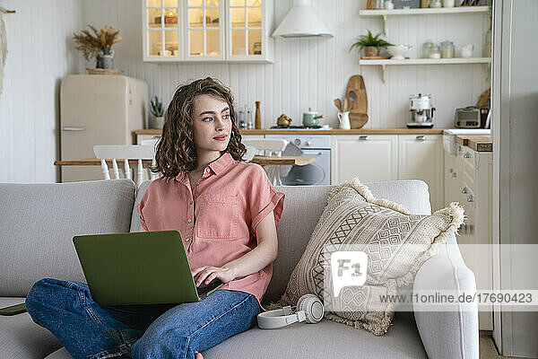 Smiling freelancer with laptop sitting on sofa at home