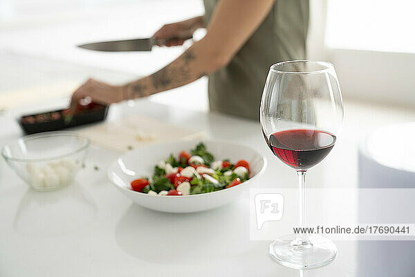 Wineglass on kitchen island with woman preparing food in background at home
