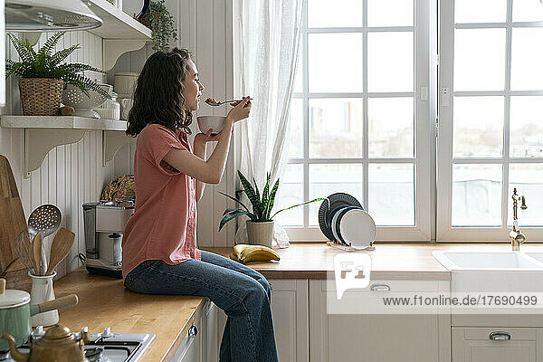 Young woman eating breakfast in kitchen at home