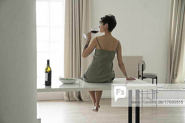 Woman drinking red wine sitting on table at home
