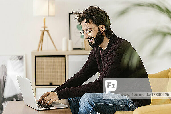 Happy man wearing eyeglasses using laptop at home