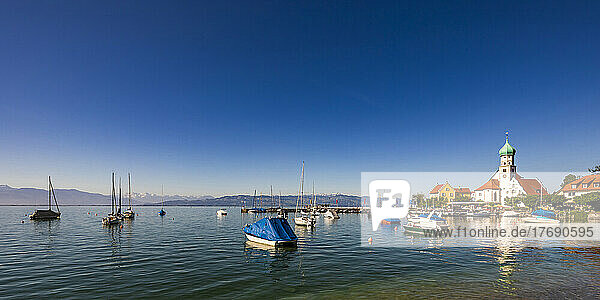 Germany  Bavaria  Wasserburg am Bodensee  Clear blue sky over boats floating in Lake Constance with Church of Saint George in background