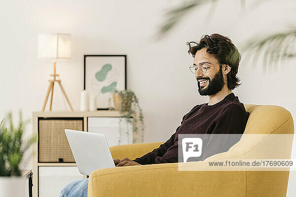 Smiling man using laptop sitting on sofa at home