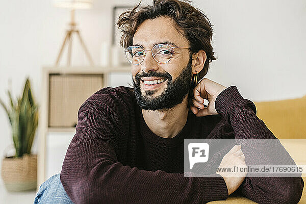 Happy man with beard sitting by sofa in living room at home