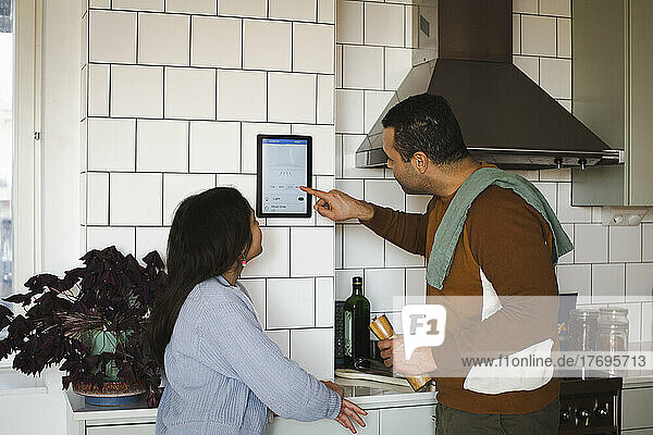 Mädchen schaut Vater an  der in der Küche zu Hause ein Hausautomatisierungsgerät benutzt