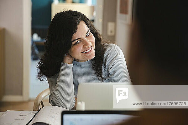 Lächelnde Frau mit Hand im Haar  die zu Hause am Laptop sitzt