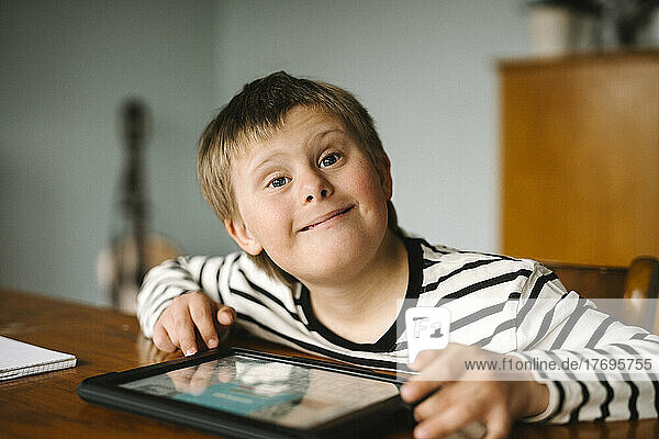 Porträt eines glücklichen Jungen mit Down-Syndrom  der am Tisch sitzt