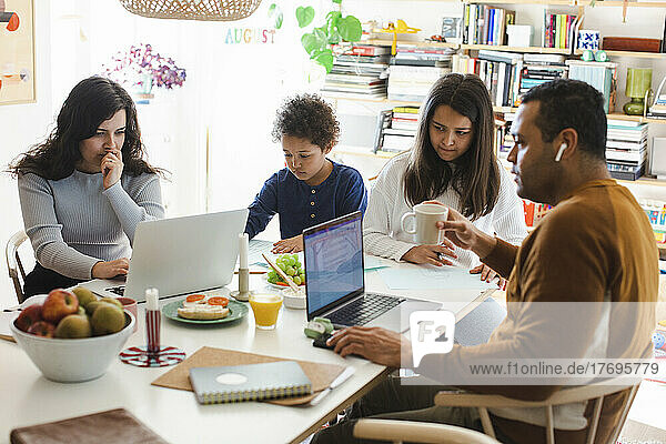 Eltern arbeiten am Laptop  während sie mit Sohn und Tochter am Tisch sitzen