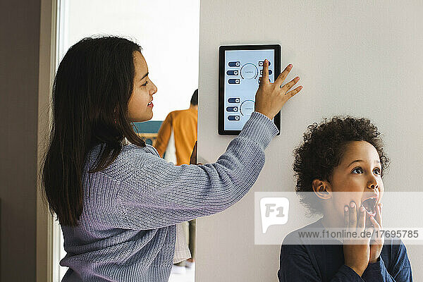 Girl using home automation device while standing with surprised brother against wall at home
