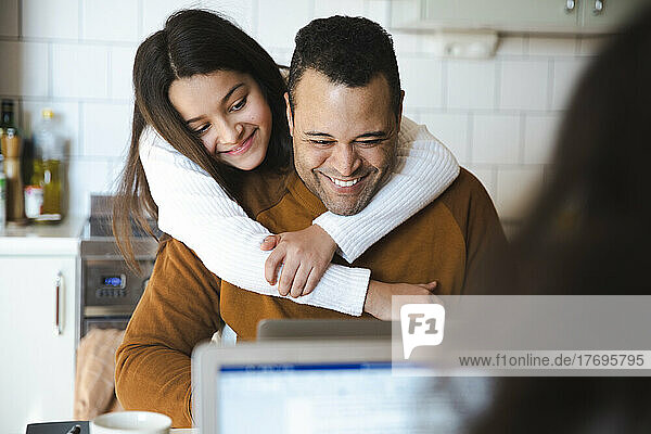 Smiling girl embracing father working on laptop at home