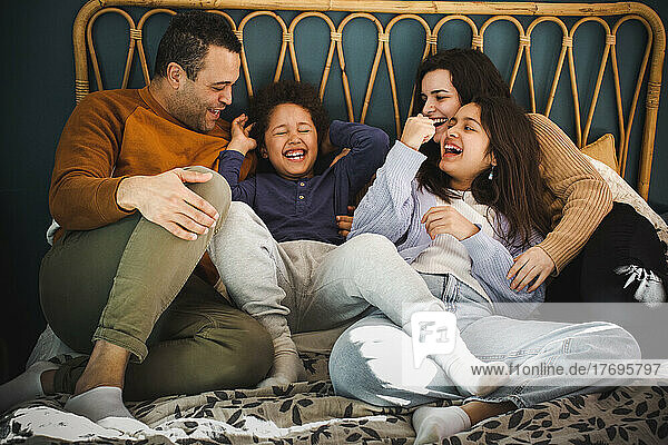 Glückliche Familie  die gemeinsam auf dem Bett sitzend zu Hause genießt