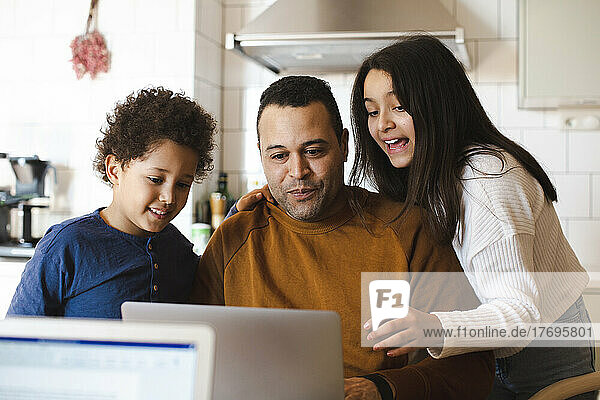Sohn und Tochter schauen mit ihrem Vater zu Hause auf den Laptop