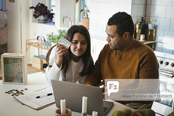Father teaching online shopping to daughter on laptop at home