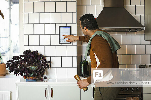 Seitenansicht eines Mannes  der ein Hausautomatisierungsgerät an der Wand benutzt  während er in der Küche steht