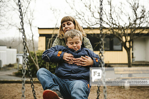 Sohn mit Down-Syndrom nimmt die Hilfe seiner Mutter in Anspruch  während er im Park auf einer Schaukel sitzt