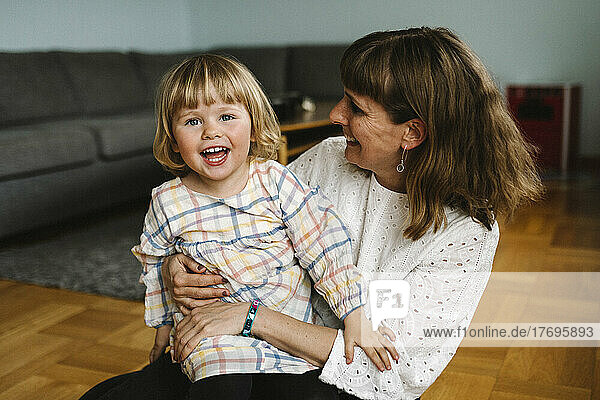 Porträt einer glücklichen Tochter mit ihrer Mutter  die zu Hause im Wohnzimmer sitzt